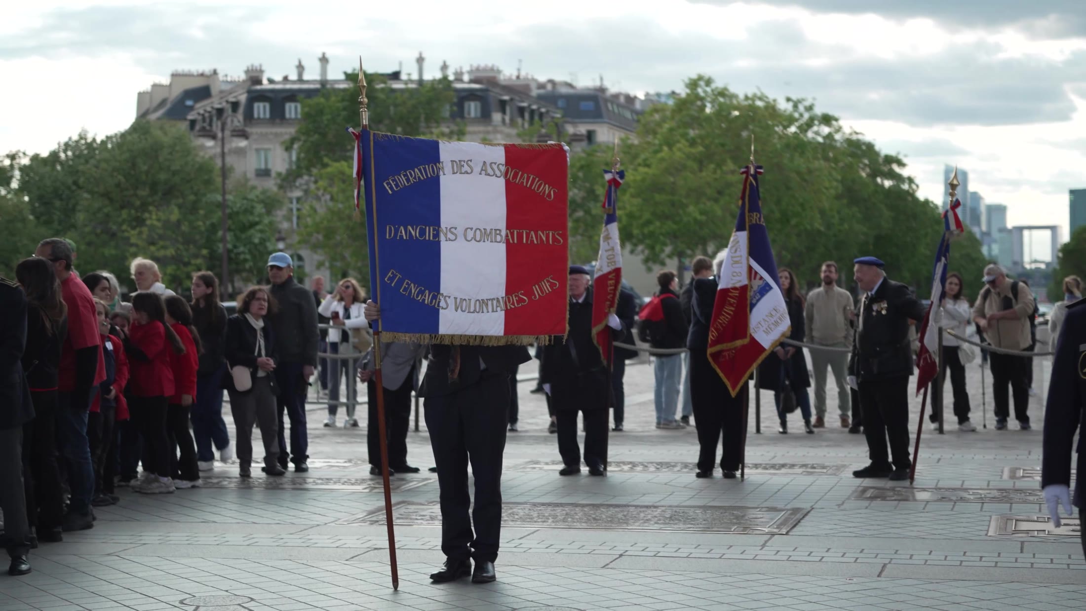 Porte-drapeau tenant la bannière de la Fédération des associations d’anciens combattants et engagés volontaires juifs, entouré d’autres porte-étendards, lors de la cérémonie à l’Arc de Triomphe en mai 2026.